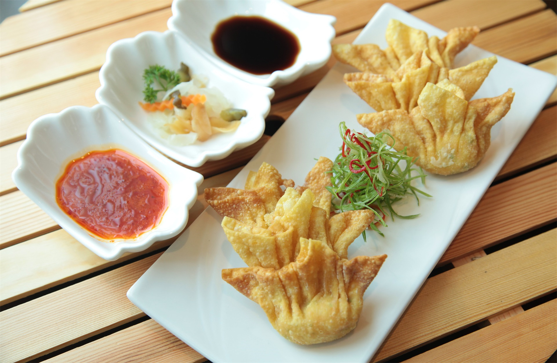 Deep-fried wontons and dipping sauces on a wooden slatted table