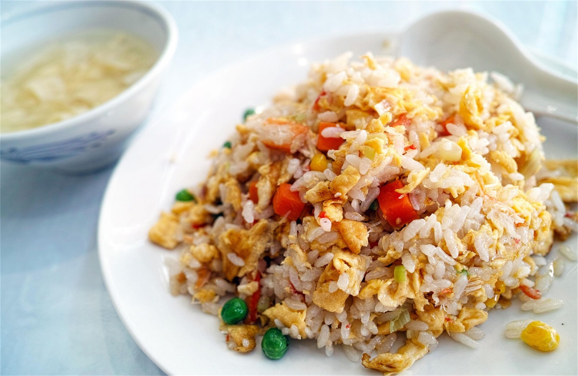 Egg fried rice with peas and carrots, with soup in the background