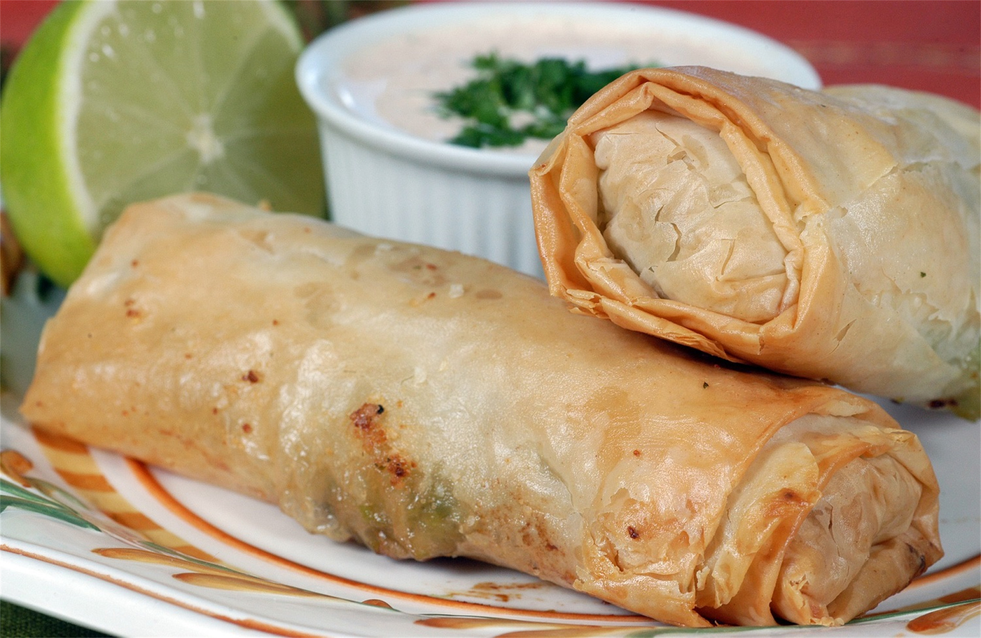 Golden crispy spring rolls, one broken open, with lime and dipping sauce